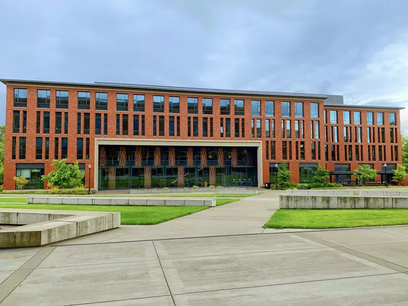 A modern red-brick teaching block with a glass entrance and a paved square in front.
