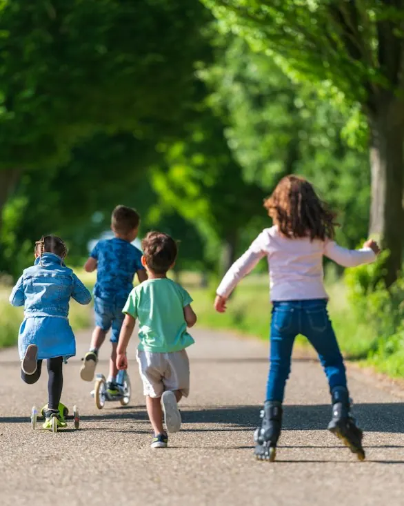 Four children running along a tree-lined path, seen from behind.