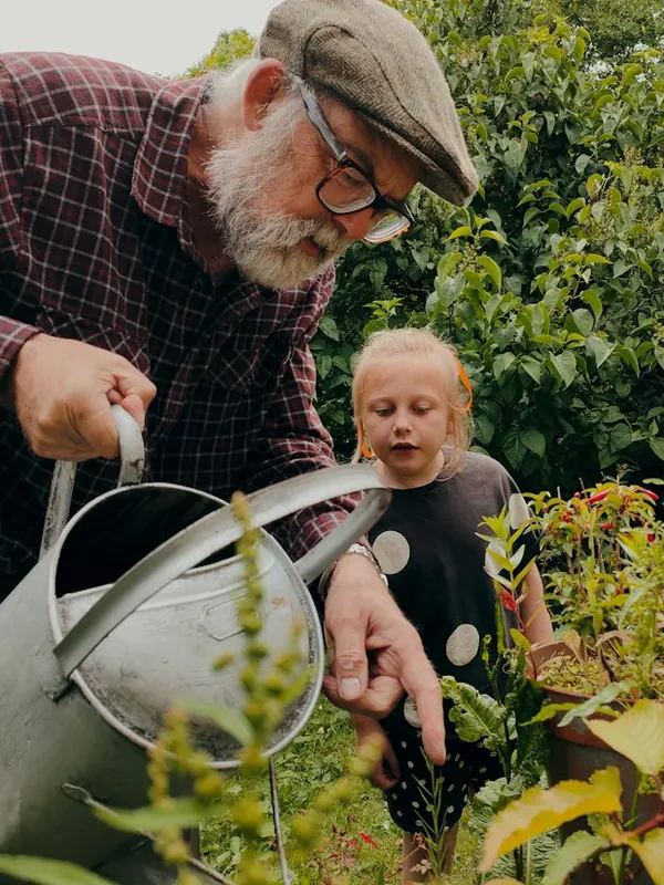 An older man and a child watering garden plants with a metal can.