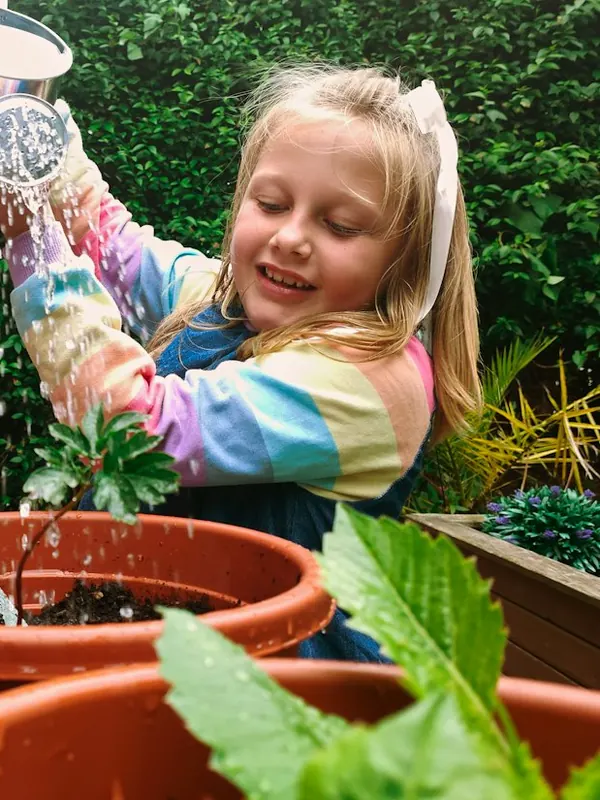 A girl in a rainbow jumper watering potted plants, with an adult beside her.